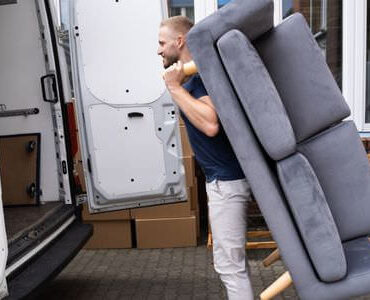 Möbellift Ratingen: Helfer tragen ein graues Sofa aus einem Transporter